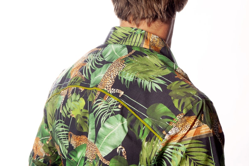 May include: A black button-down shirt with a tropical print featuring green leaves and leopard spots. The shirt has a yellow trim around the collar and down the front.