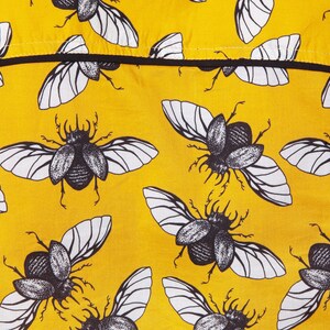 May include: Yellow fabric with a repeating pattern of black and white beetle illustrations. The beetles have wings and are drawn in a vintage style.