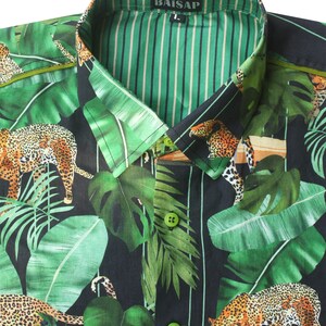 May include: A black and green button-up shirt with a jungle print featuring leopards and palm leaves. The shirt has a green and white striped inner collar and the brand name "BAISAP" is printed on the collar.
