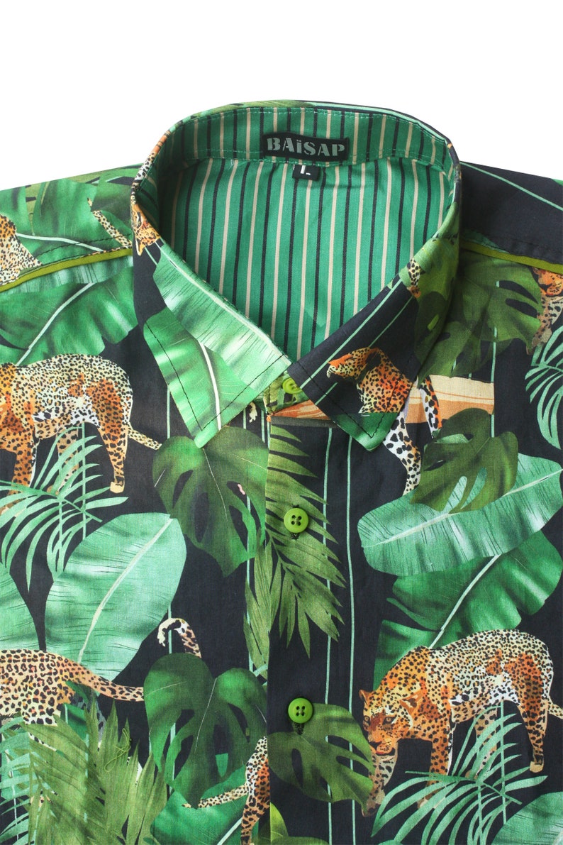 May include: A black and green button-up shirt with a jungle print featuring leopards and palm leaves. The shirt has a green and white striped inner collar and the brand name "BAISAP" is printed on the collar.
