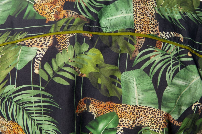 May include: A black fabric with a green and brown jungle print featuring leopards and tropical leaves.