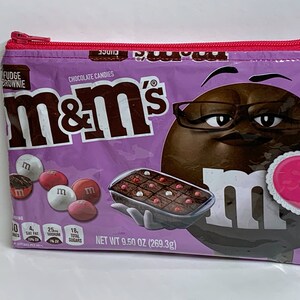 May include: A purple zippered pouch featuring M&M's Fudge Brownie branding. The pouch displays a brown M&M character wearing glasses and holding a heart. The pouch is 9.50 oz (269.3g).