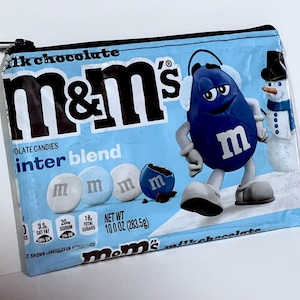 May include: A zippered pouch featuring a light blue M&M's Winter Blend design. The pouch displays the M&M's logo, a blue M&M's character with earmuffs, and a snowman. The pouch is 10 oz (283.5g).
