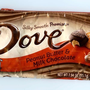 May include: A brown and gold zippered pouch with the Dove logo and the text "Silky Smooth Promises® Dove Peanut Butter & Milk Chocolate Net Wt 7.94 oz 225.1g".