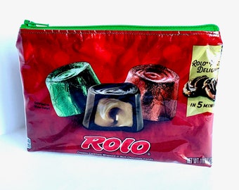May include: A red zippered pouch with a ROLO candy bar design. The pouch features three ROLO candies, one green, one red, and one brown. The text "ROLO DELIGHT IN 5 MIN" is printed on the pouch.