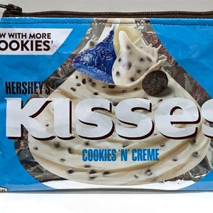 May include: A blue zippered pouch with a Hershey's Kisses Cookies 'n Creme design. The pouch features a white chocolate kiss with chocolate chips and a chocolate cookie.