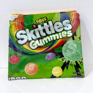 May include: A green zippered pouch featuring the text "SOUR Skittles Gummies" in white. The pouch has a rainbow design and includes images of colorful gummy candies. The pouch is rectangular and has a yellow zipper.