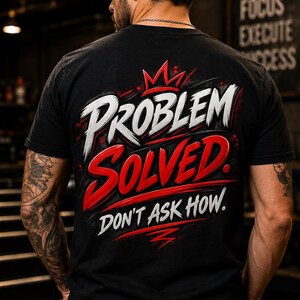 May include: A black short-sleeved t-shirt featuring a graphic design on the back. The text reads "PROBLEM SOLVED" in large white and red stylised lettering, topped with a red crown icon, and the phrase "DON'T ASK HOW." in white below it.