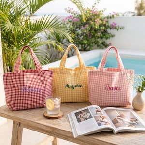 Puede incluir: Tres bolsos de tela con estampado de cuadros vichy en rojo, amarillo y rosa claro. Cada bolso tiene un nombre bordado en la parte delantera: Kristin en morado, Marjorie en verde y Janice en rosa. Los bolsos tienen dos asas y base rectangular.
