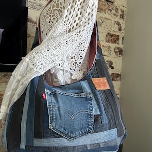 Peut inclure: Un sac à bandoulière de style hobo fabriqué à partir de bandes de jean en patchwork dans des nuances variées de bleu et de noir. Le sac présente une poche extérieure en jean avec une étiquette rouge Levi's et un écusson en cuir beige.