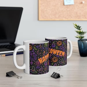 May include: Two white ceramic mugs featuring a black background with a colorful neon-style pattern of cats, pumpkins, witch hats, and spiderwebs. The text HAPPY HALLOWEEN is printed in bold orange letters across the front of the mugs.