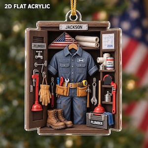 May include: A 2D flat acrylic ornament featuring a locker interior with the name JACKSON, a blue plumber uniform, work boots, a tool belt, and various plumbing tools including a wrench, plunger, and pipe cement. The design includes an American flag.
