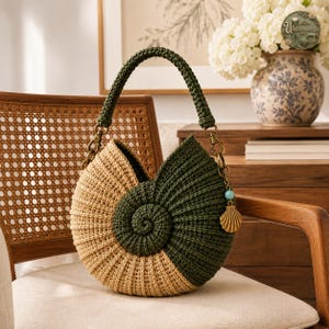 May include: A round, spiral-shaped crochet bag featuring a two-tone design in beige and dark green. The bag has a matching dark green crocheted handle attached with brass-toned metal hardware, including a small turquoise bead and a shell charm.