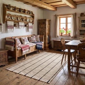 May include: A rectangular woven area rug featuring a cream-colored base with thin, evenly spaced black vertical stripes and a fringed edge, positioned on a wooden floor in a room with a wooden bench, table, chairs, and a tiled stove.