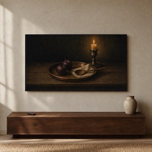 May include: A framed wall art print depicting a dark still life scene with two dark purple plums on a round metal tray, a wooden spoon resting on a piece of fabric, and a single lit candle in a metallic holder, all set on a wooden surface.