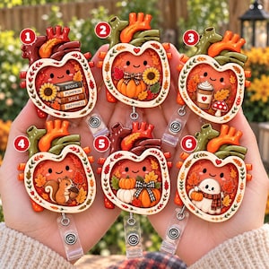 May include: Six heart-shaped badge reels featuring autumn themes. Design 1 shows books, 2 a pumpkin, 3 a coffee cup, 4 a squirrel, 5 pumpkins with a bow, and 6 a ghost. Each anatomical heart illustration has a smiling face and fall foliage.