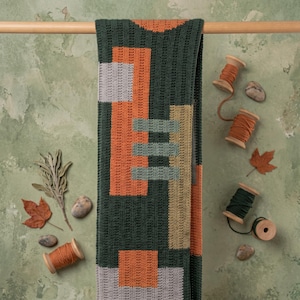 May include: A rectangular crochet blanket featuring a dark green base with geometric blocks in burnt orange, light gray, and tan. The pattern consists of vertical and horizontal rectangular shapes arranged in a structured, repeating design.