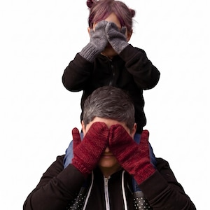Könnte beinhalten: Ein Paar dunkelgraue Strickfäustlinge und ein Paar tiefrote Strickfäustlinge. Die grauen Fäustlinge bedecken ein Gesicht, die roten Fäustlinge bedecken ein weiteres Gesicht. Beide Paare sind mit einem gerippten Bündchen am Handgelenk versehen.