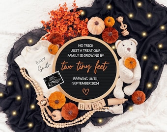 以下が含まれることがあります： NO TRICK JUST A TREAT OUR FAMILY IS GROWING BY two tiny feet BREWING UNTIL SEPTEMBER 2024という文字が書かれた黒い円形のレターボード。白いベビー用ボディスーツ、かぎ針編みのテディベア、オレンジ色のカボチャ、木製のビーズに囲まれています。