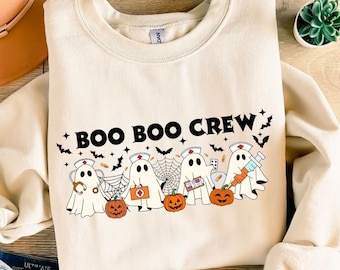 以下が含まれることがあります： BOO BOO CREWという黒いグラフィックがプリントされたクリーム色のクルーネックトレーナー。聴診器、医療キット、クリップボード、注射器を持った医療従事者の格好をした4体の幽霊と、カボチャやコウモリが描かれています。