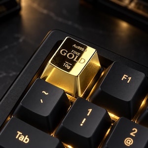 May include: A metallic gold-colored keycap shaped like a small bullion bar, featuring the engraved text Au999.9, FINE GOLD, and 10g, installed on a black mechanical keyboard among standard black keycaps with backlit gold-colored characters.