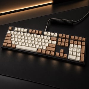 Peut inclure: Un clavier mécanique pleine taille avec un cadre noir et des touches bicolores, comprenant des touches alphanumériques crème et des touches de modification marron clair. Un câble noir torsadé est branché sur le haut du clavier.