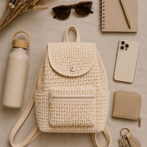 Puede incluir: Una mochila de ganchillo color crema con un bolsillo frontal con cremallera y un cierre de solapa con un broche plateado. Los artículos circundantes incluyen una botella de agua beige, gafas de sol de carey, un cuaderno de espiral, un bolígrafo, un teléfono inteligente, una cartera y llaves.