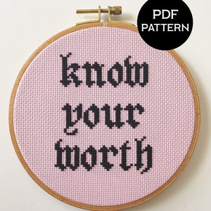 May include: A pink embroidery hoop with the phrase "know your worth" stitched in black gothic font. The hoop is made of wood and has a brass screw.