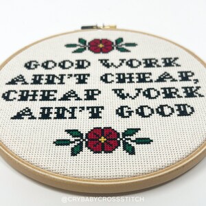 May include: A white embroidery hoop with a cross-stitch design that reads "Good work ain't cheap, cheap work ain't good". The design is in black thread with red and green accents.