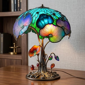 May include: A table lamp featuring a stained glass shade with a vibrant floral pattern in shades of turquoise, purple, and orange. The base is crafted from bronze-toned metal, sculpted to resemble tree roots with small, colorful glass accents.