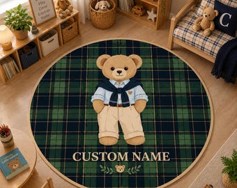 May include: A round area rug featuring a dark green and navy blue plaid pattern. In the center, a light brown teddy bear wears a light blue striped shirt, a navy blue sweater draped over the shoulders, and beige trousers. The text CUSTOM NAME is printed below.