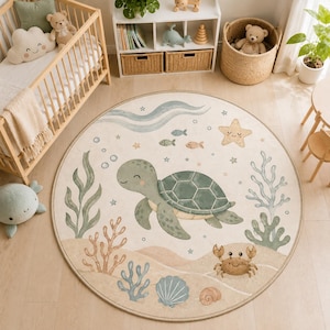 Op de afbeelding: Een rond vloerkleed met een lichtbeige achtergrond en een centrale illustratie van een groene zeeschildpad, omringd door aquarelachtige zeedieren zoals een krab, een zeester, schelpen, koraal, zeewier en kleine vissen in zachte pasteltinten.