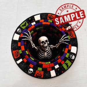 May include: A circular rug featuring a central skeleton with raised arms emerging from a black void. The border consists of a colorful mosaic-style pattern of squares in orange, purple, green, and white, interspersed with icons of skulls, bats, and pumpkins.