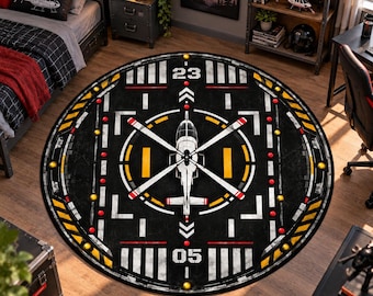 Op de afbeelding: Een rond vloerkleed met een zwart helikopterlandingsplaatsontwerp met witte markeringen, gele accenten en de cijfers 23 en 05. De afbeelding bevat een centrale helikopterillustratie met witte rotorbladen op een donkere achtergrond.