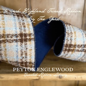 May include: A 4 inch wide Highland Tweed ribbon featuring a plaid pattern in shades of tan, light blue, and brown with a solid dark navy blue interior. The text reads 4 inch Highland Tweed Ribbon By The Yard, PEYTON ENGLEWOOD Curated Ribbon Library, Haddonfield, NJ.