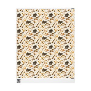May include: A rectangular sheet of paper featuring a repeating pattern of snakes in various poses, including coiled and slithering, rendered in shades of black, brown, and tan against a cream background, interspersed with small green leaf sprigs.