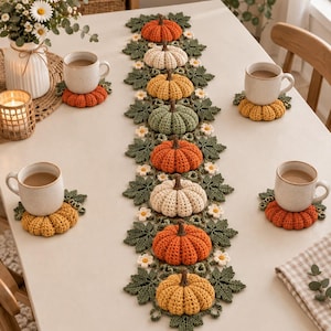 Può includere: Un lungo runner da tavola all'uncinetto con una fila centrale di zucche imbottite nei colori arancione, crema, giallo e verde salvia, circondate da foglie all'uncinetto verde scuro e piccoli fiori bianchi. Quattro sottobicchieri a zucca.