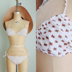 May include: White bikini with a red and blue geometric print. The bikini top is a triangle style and the bottom has tie sides.