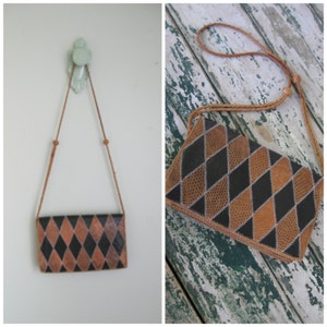 Peut inclure: Un sac à main rectangulaire avec un motif de losanges marron et noir. Le sac a une longue et fine bandoulière marron et est suspendu à un mur. Le motif du sac est un motif répété de losanges marron et noirs.