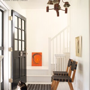 Pode incluir: Um corredor branco com uma porta preta, um tapete listrado preto e branco e duas cadeiras de madeira com assentos tecidos pretos. As paredes s&atilde;o pintadas de "White Dove OC-17" com acabamento fosco e o rodap&eacute; &eacute; pintado de "Aura Satin".