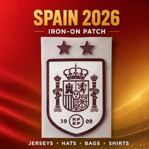 Könnte beinhalten: Ein Aufbügler mit dem Spanien 2026 Wappen in Dunkelrot auf weißem Hintergrund. Das Design umfasst ein zentrales Wappen mit Krone, zwei Sternen darüber und dem Text 1909 RFEF. Der Aufnäher ist auf einem rechteckigen weißen Trägermaterial abgebildet.