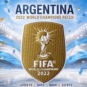 Puede incluir: Un parche dorado en forma de escudo con el icono del trofeo FIFA World Champions, el texto FIFA WORLD CHAMPIONS 2022 y el encabezado ARGENTINA 2022 WORLD CHAMPIONS PATCH. El texto inferior enumera JERSEYS, HATS, BAGS, SHIRTS.