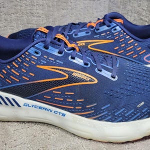 Könnte beinhalten: Ein Paar marineblaue Brooks Glycerin GTS 20 Laufschuhe mit orangefarbenen Akzenten an den Seiten und Schnürsenkeln. Die Schuhe verfügen über eine weiße Zwischensohle, ein Mesh-Obermaterial mit orangefarbenen Details und den Schriftzug Brooks und Glycerin GTS an der Seite.