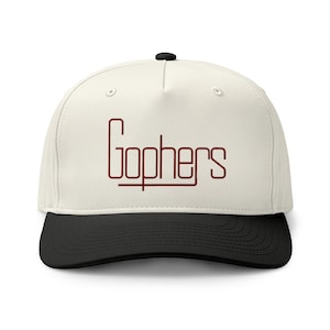 May include: A five-panel baseball cap with an off-white crown and a solid black brim. The front of the cap features the word Gophers printed in a dark red, thin, stylised sans-serif font with a horizontal line extending from the letter G.