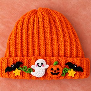 May include: A bright orange ribbed knit beanie featuring a wide folded cuff decorated with crocheted appliques including a white ghost, an orange jack-o'-lantern, two black bats, and two small yellow stars connected by green vine-like accents.