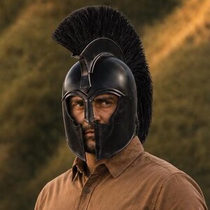 May include: A black Spartan-style helmet featuring a prominent, tall black crest made of stiff bristles. The helmet has a smooth, dark finish with a T-shaped face opening that exposes the eyes and nose area, covering the sides and top of the head.