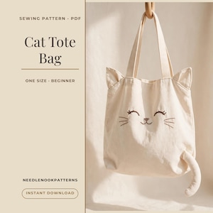 以下が含まれることがあります： 2つの持ち手、猫耳、刺繍された猫の顔が付いたベージュのキャンバストートバッグ。テキストには「SEWING PATTERN PDF, Cat Tote Bag, ONE SIZE BEGINNER, NEEDLENOOKPATTERNS, INSTANT DOWNLOAD」と書かれています。バッグには小さな尻尾が付いています。