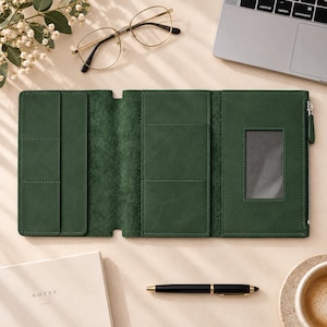 Puede incluir: Un organizador de cartera de tres pliegues en color verde oscuro con múltiples ranuras para tarjetas, una ventana transparente para identificación y un compartimento lateral con cremallera. El interior muestra un acabado texturizado con bordes cosidos.