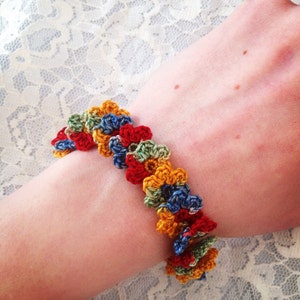 Könnte beinhalten: Ein farbenfrohes gehäkeltes Armband mit einem Blumendesign in Rot-, Gelb-, Blau- und Grüntönen.