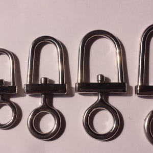 Op de afbeelding: Vijf zilverkleurige metalen draaibare karabijnsluitingen op een rij van klein naar groot. Elke sluiting heeft een U-vormige lus bevestigd aan een rechthoekige basis met een ronde draairing aan de onderkant, met een gepolijste metalen afwerking.